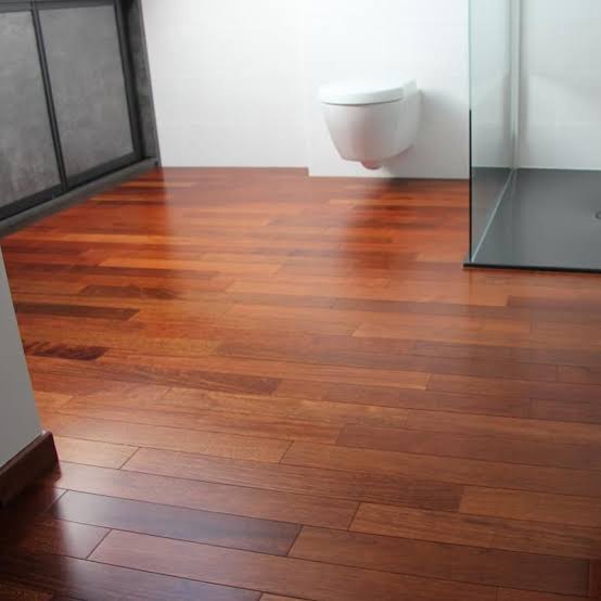 Modern bathroom featuring polished reddish-brown Merbau wood flooring, a wall-mounted toilet, and a glass shower enclosure.